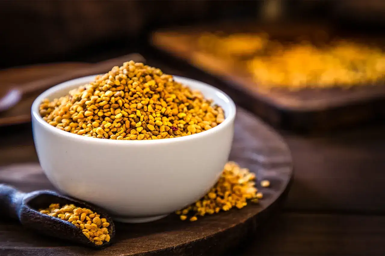 Złocisty pyłek pszczeli w miseczce i drewnianej łyżce. Dowiedz się, jak stosować pyłek pszczeli dla zdrowia.