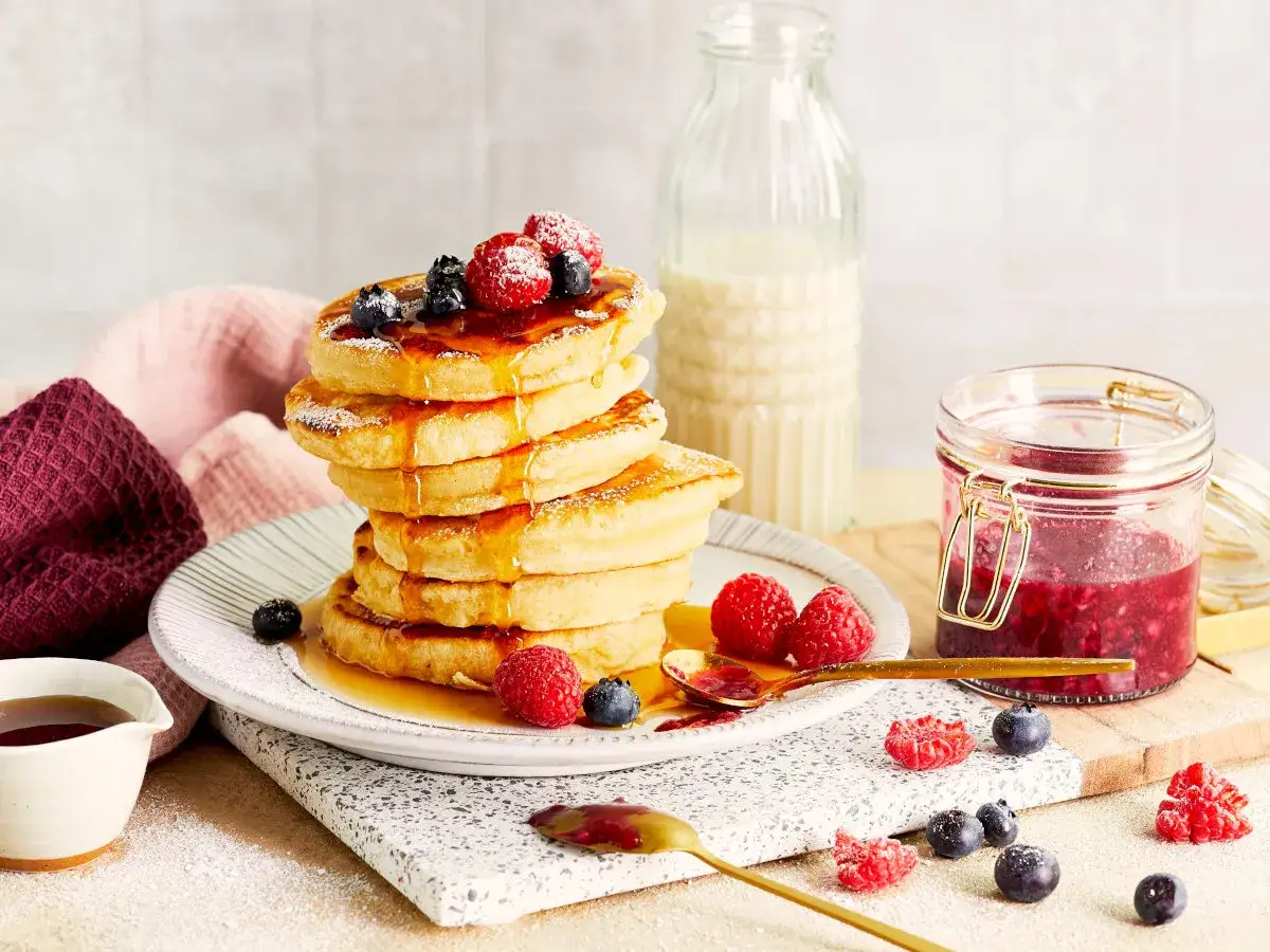 Puszyste proteinowe pancakes z malinami i borówkami, polane syropem. Idealne na zdrowe śniadanie, jak zrobic proteinowe pancakes.