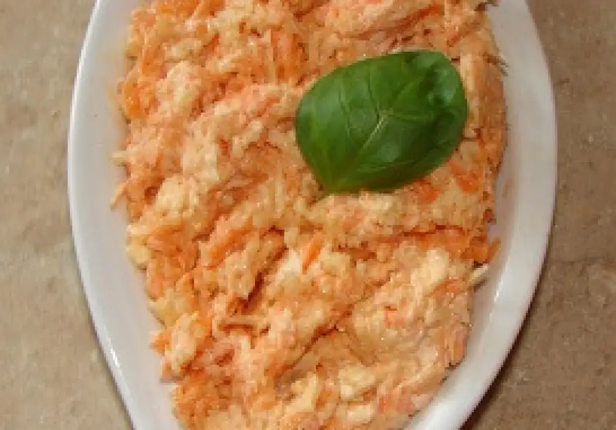 Surówka z tartej marchewki z jabłkiem i chrzanem, podana na białym talerzu, ozdobiona listkiem bazylii.