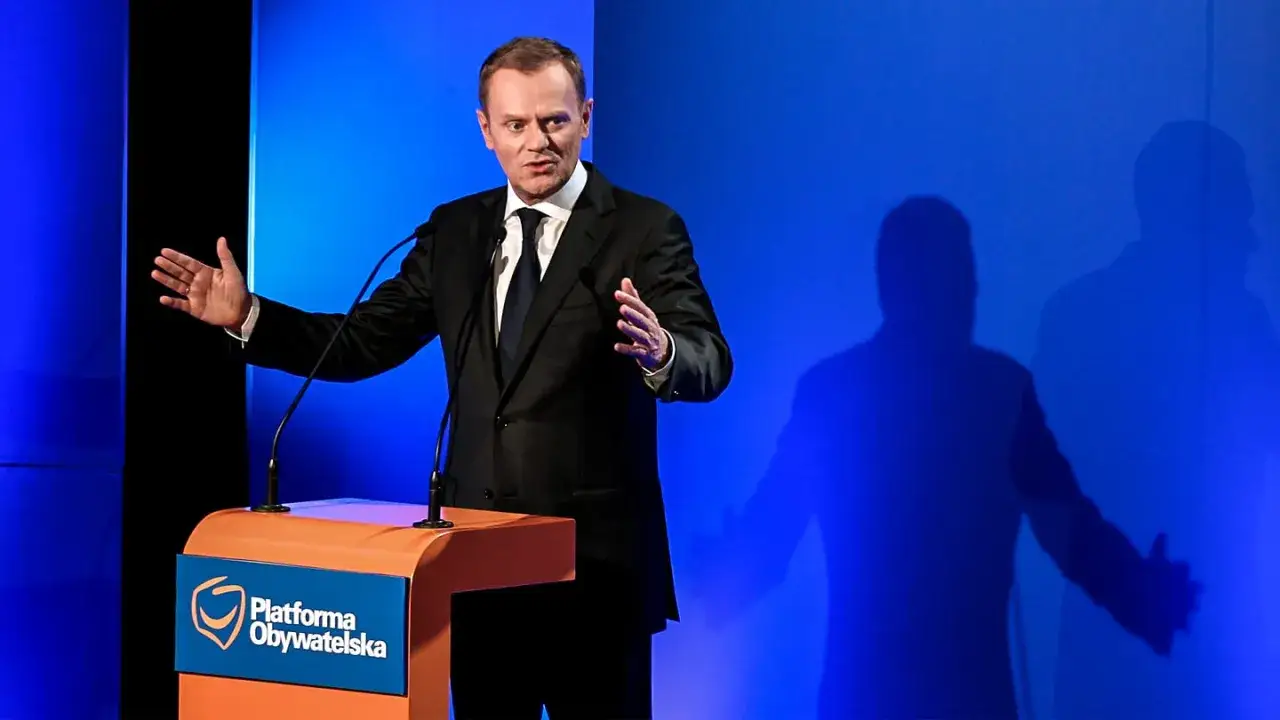 Donald Tusk przemawia na tle niebieskiej ściany, z logo Platformy Obywatelskiej.