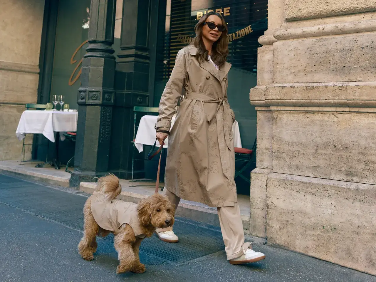 Kobieta w jasnym płaszczu i spodniach spaceruje z psem. Stylowa stylizacja na co dzień.