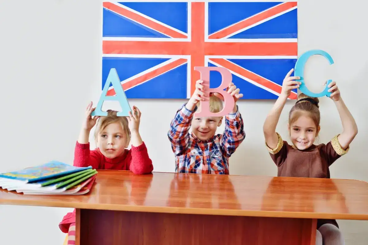 Dzieci uczą się angielskiego przez zabawę, trzymając litery A, B, C na tle flagi Wielkiej Brytanii.