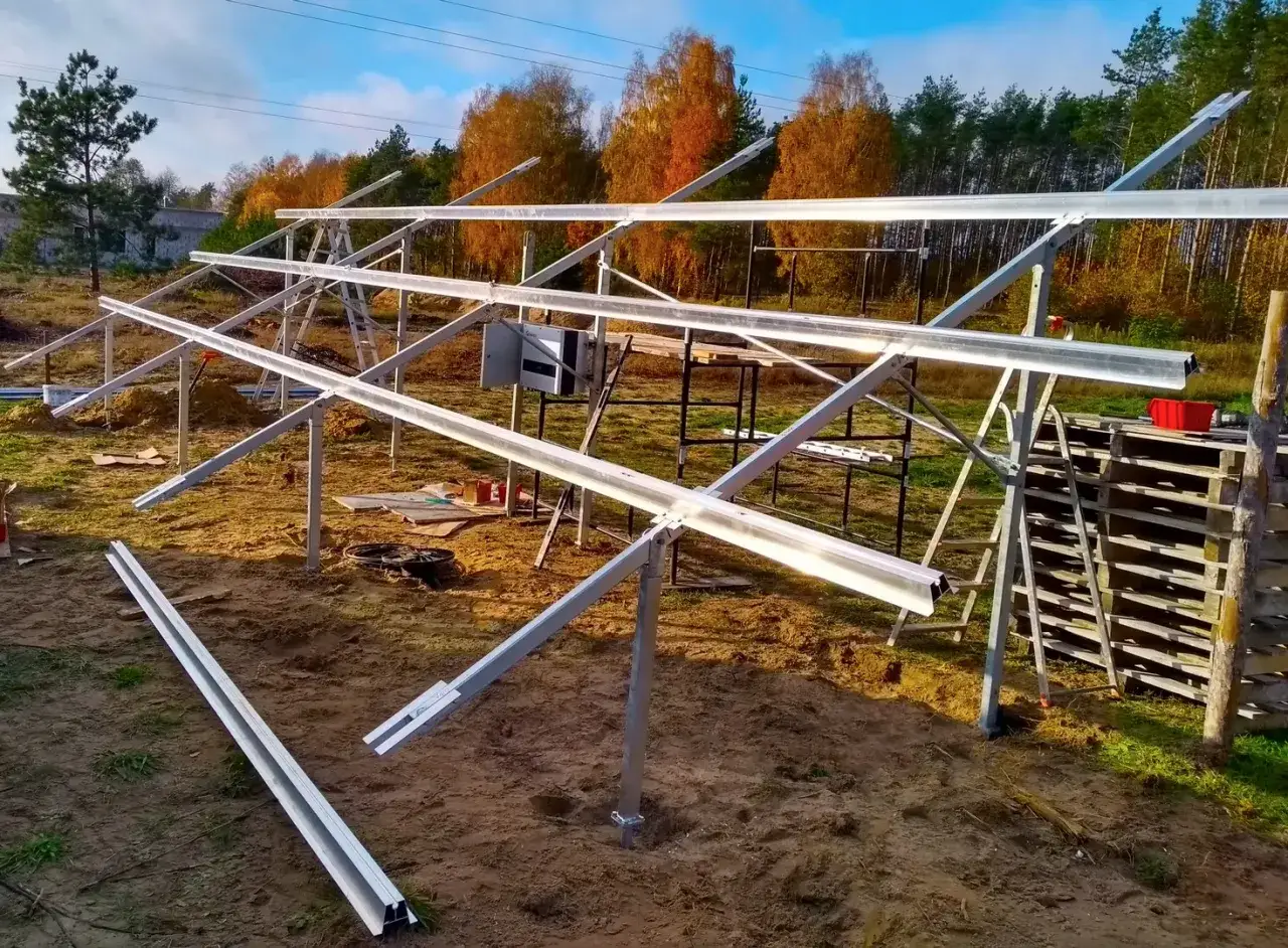 Budowa konstrukcji, jak zrobić stelaż pod panele fotowoltaiczne. Metalowe profile montowane na gruncie, w tle jesienne drzewa.