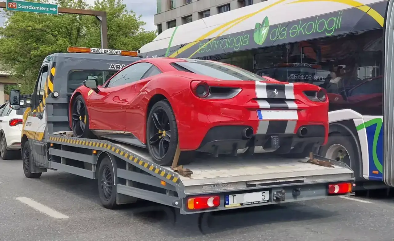 Czerwone Ferrari na lawecie, gotowe do cesji leasingu na osobę prywatną. Obok autobus z napisem 