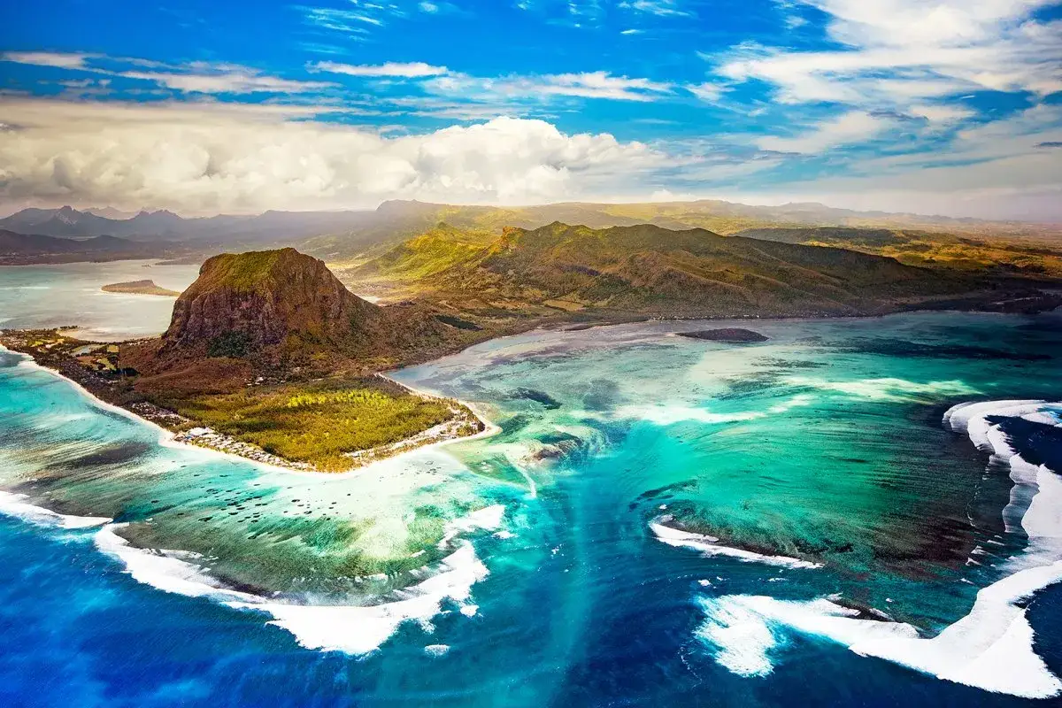 Widok z lotu ptaka na Mauritius, gdzie turkusowa woda obmywa zielone wybrzeże, a pod nią rozciąga się rafa koralowa.