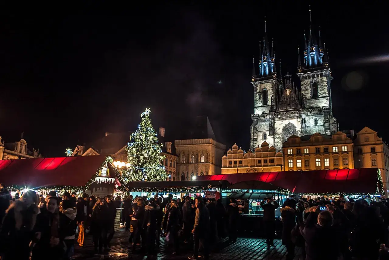 Tłumy ludzi na jarmarku bożonarodzeniowym w Pradze, podświetlona choinka i zabytkowe budynki tworzą magiczną atmosferę.