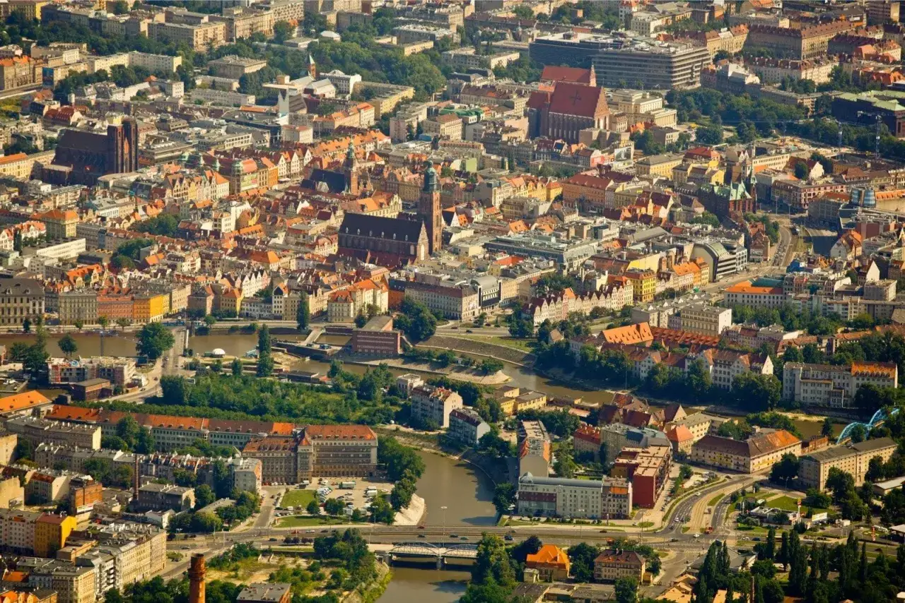 Widok z lotu ptaka na Wrocław, jedno z największych polskich miast, z rzeką przecinającą gęstą zabudowę i zabytkowe kościoły.