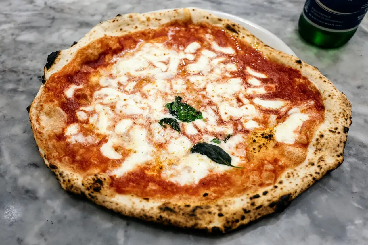 Pyszna pizza Margherita, idealna po długim leżakowaniu ciasta na pizzę. Sos pomidorowy, ciągnący ser i świeża bazylia.