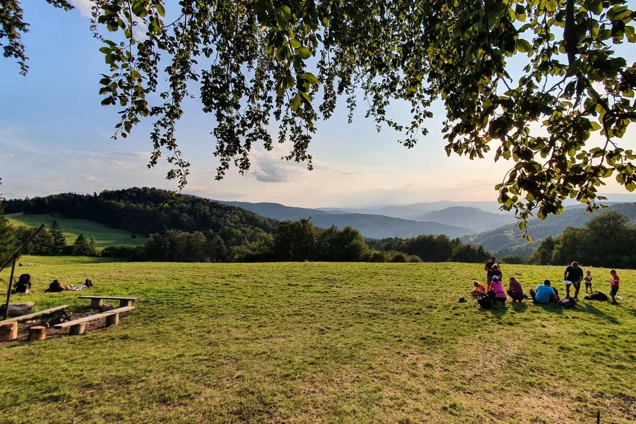 Grupa ludzi odpoczywa na trawie przy ognisku, podziwiając widok na g&oacute;ry. To idealne miejsce na odpoczynek, jak na bac&oacute;wce nad Wierchomlą.
