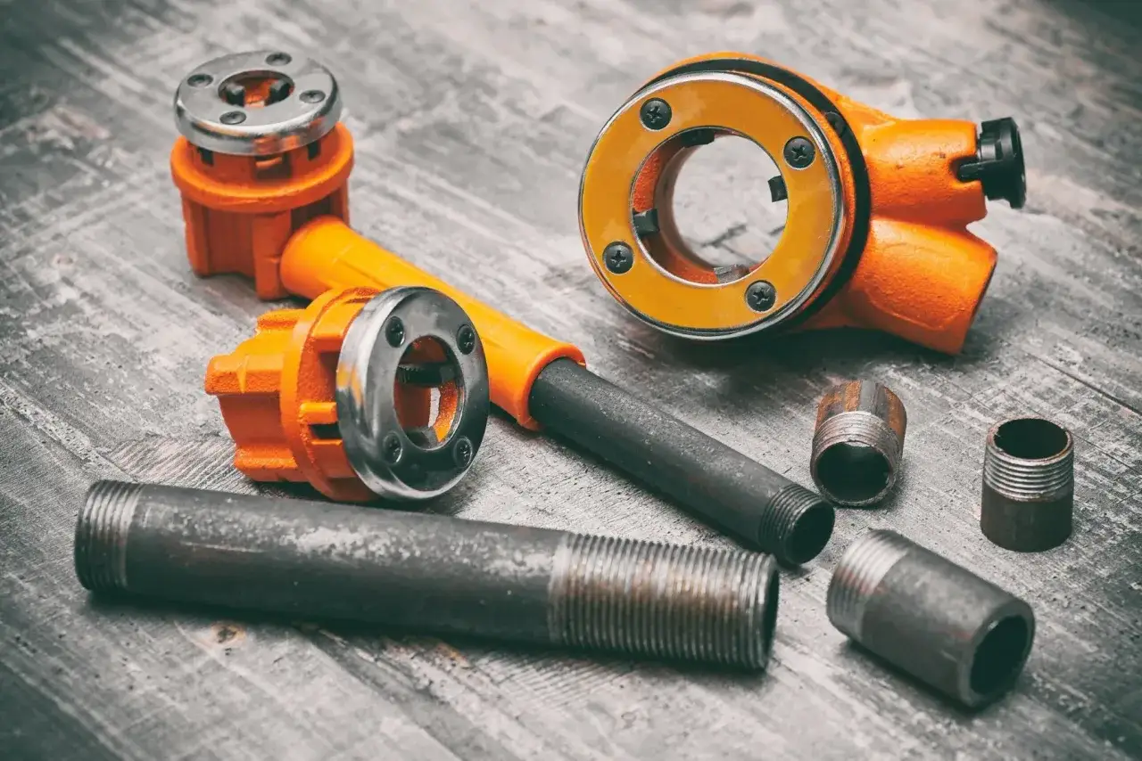 Narzędzia do gwintowania rur stalowych i przykładowe fragmenty rur. Dowiedz się, jak połączyć rury stalowe, tworząc solidne połączenia.