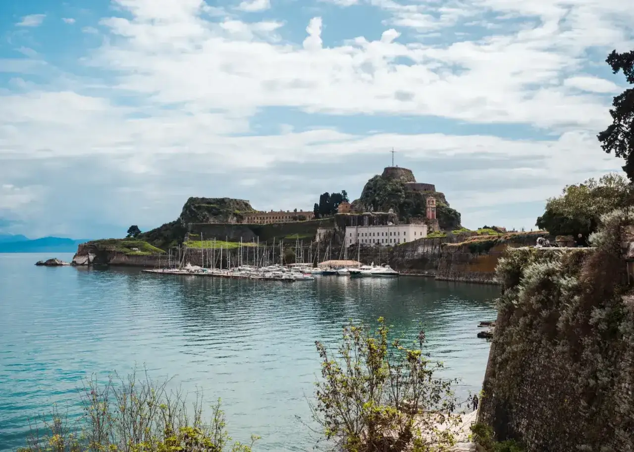 Widok na port z jachtami i starożytną fortecą na wzg&oacute;rzu. Idealne miejsce na wakacje, sprawdź korfu ceny!