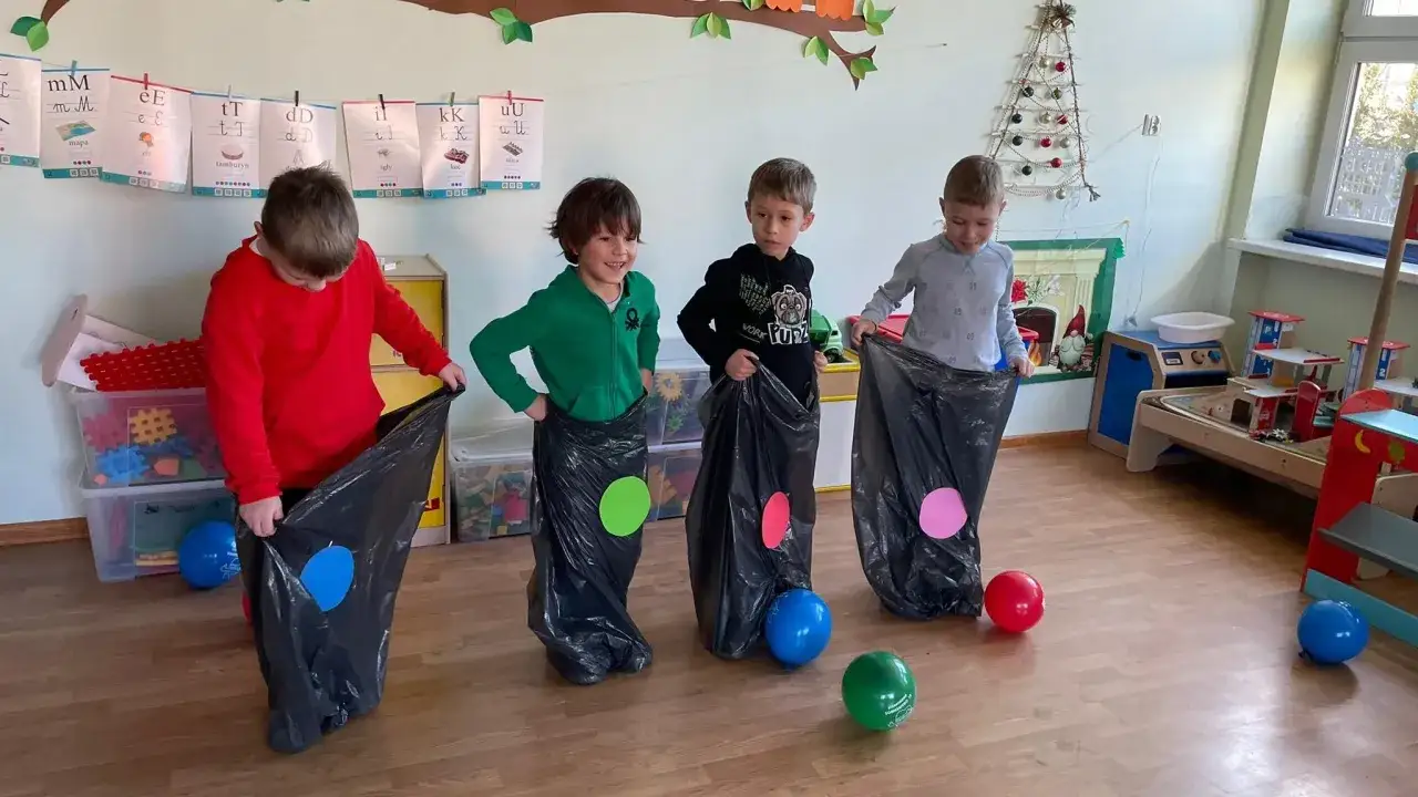 Cztery chłopców w przedszkolu, w workach po kolana, skacze w zabawie. Czy przedszkole ma ferie? Nie, to tylko zabawa!
