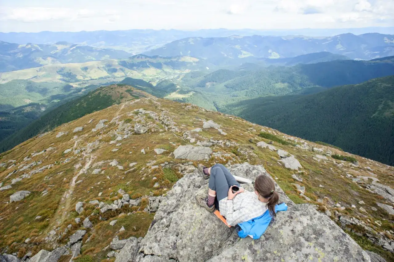 Widok na góry z odpoczywającą turystką. Idealne fajne miejsca w górach na weekend, by podziwiać panoramę i napić się kawy.