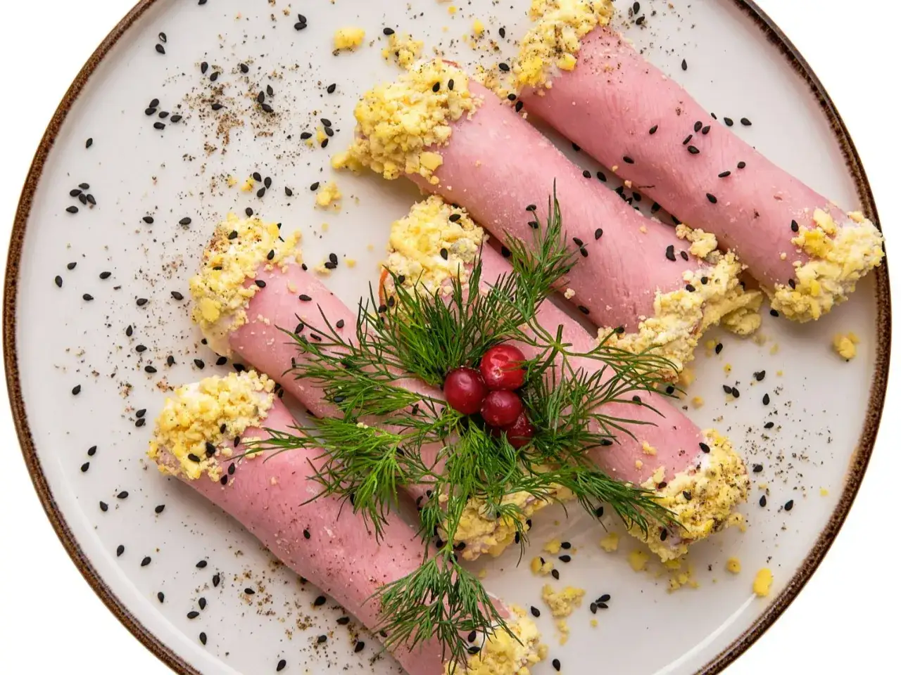 Roladki z szynki z jajeczną posypką, ozdobione koperkiem i żurawiną, posypane czarnuszką.