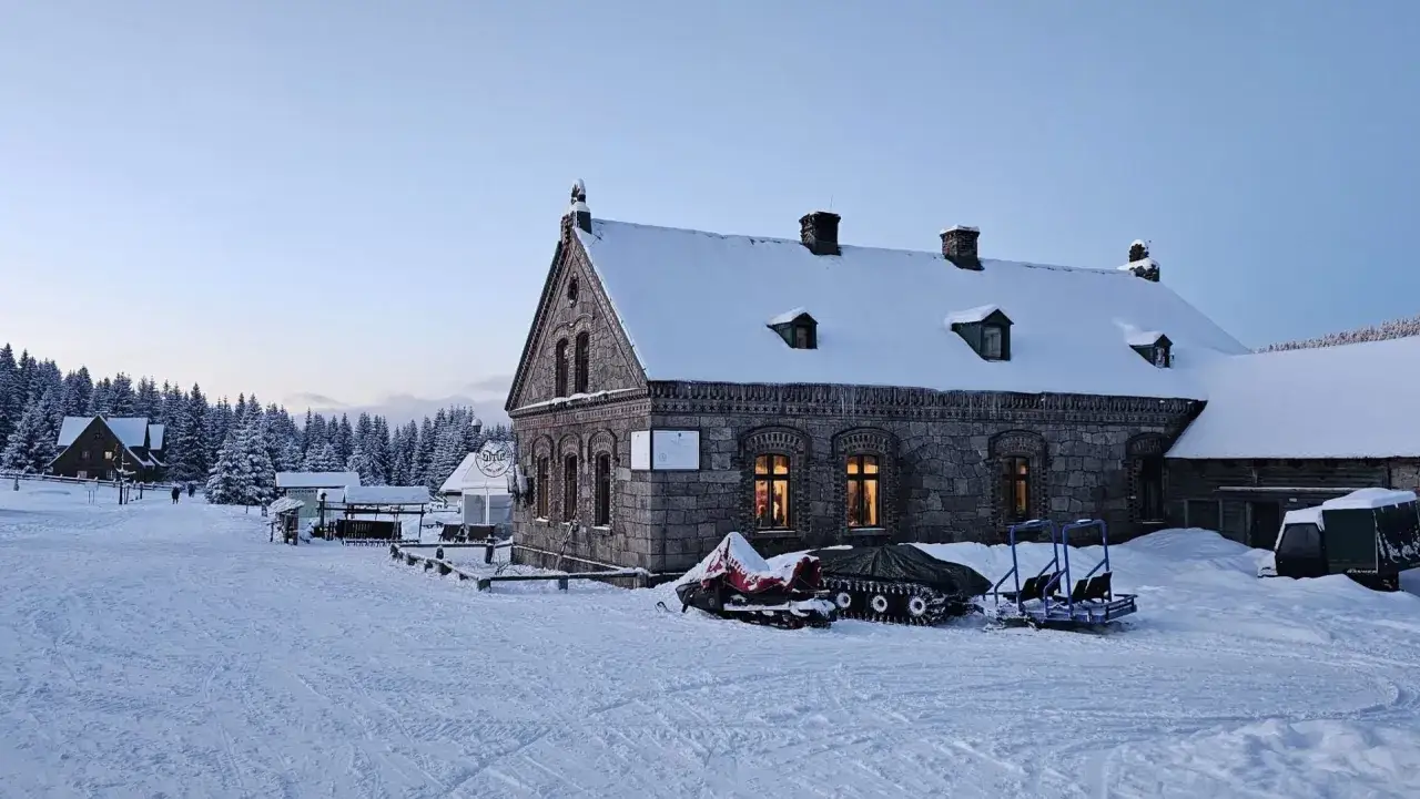 Kamienna stacja turystyczna Orle w zimowej scenerii. Śnieg pokrywa dachy i otoczenie, a w oknach widać ciepłe światło.