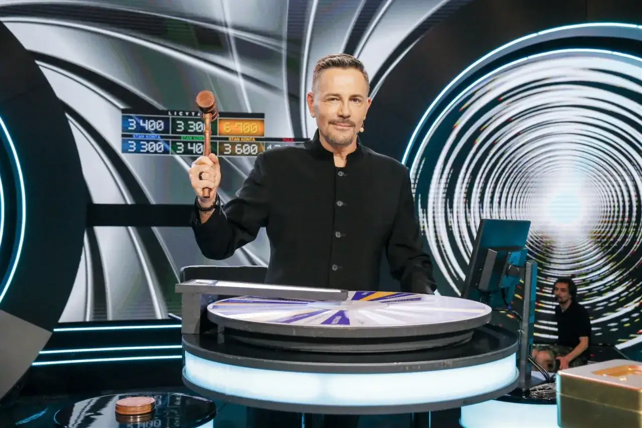 Krzysztof Ibisz z młotkiem w ręku, na tle teleturniejowego koła fortuny i ekranów z wynikami. Czy to zapowiedź jego majątku?