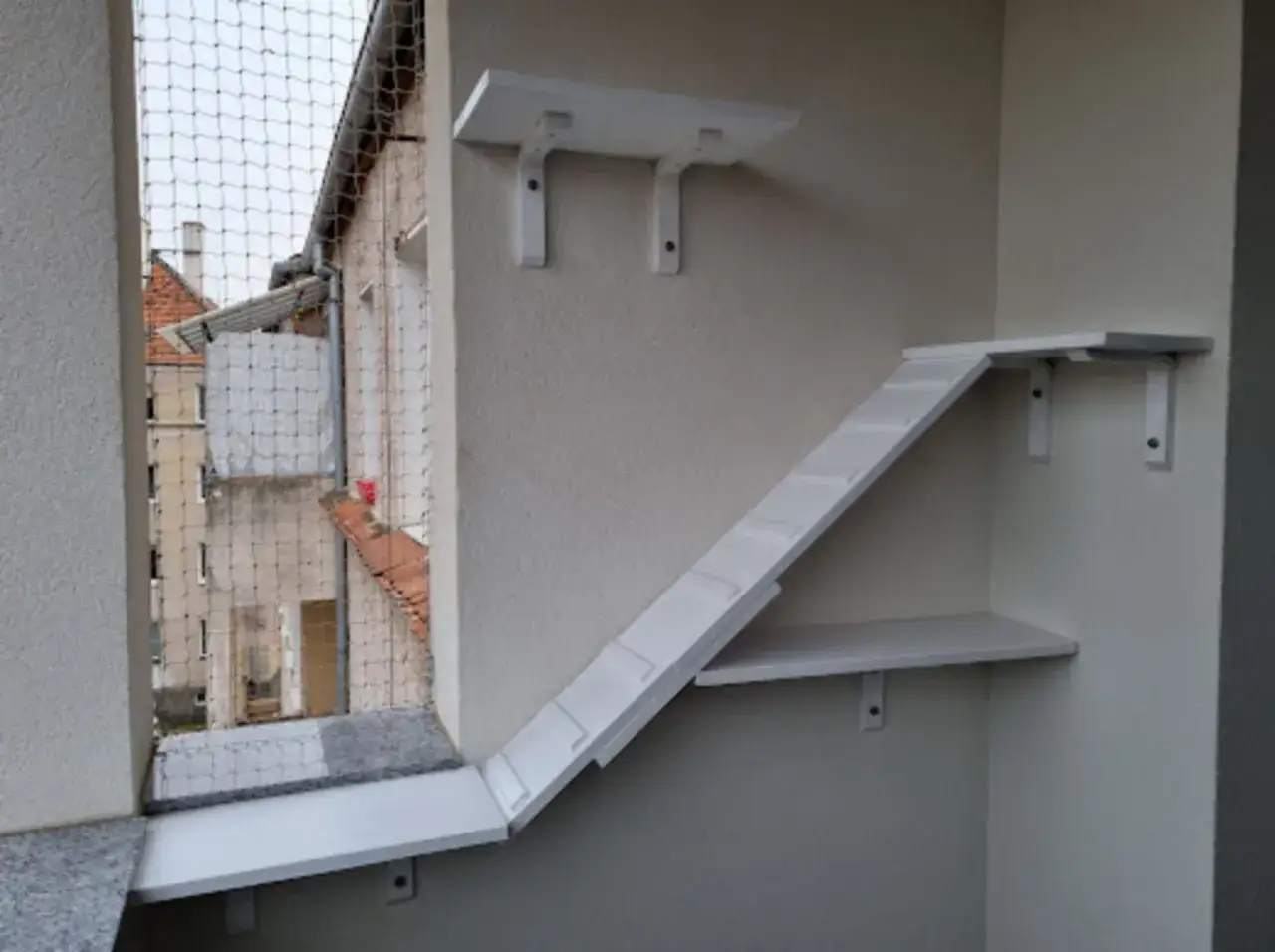 Biała półka dla kota na balkon, z rampą i dodatkowymi platformami, tworzy bezpieczną przestrzeń do zabawy i obserwacji.