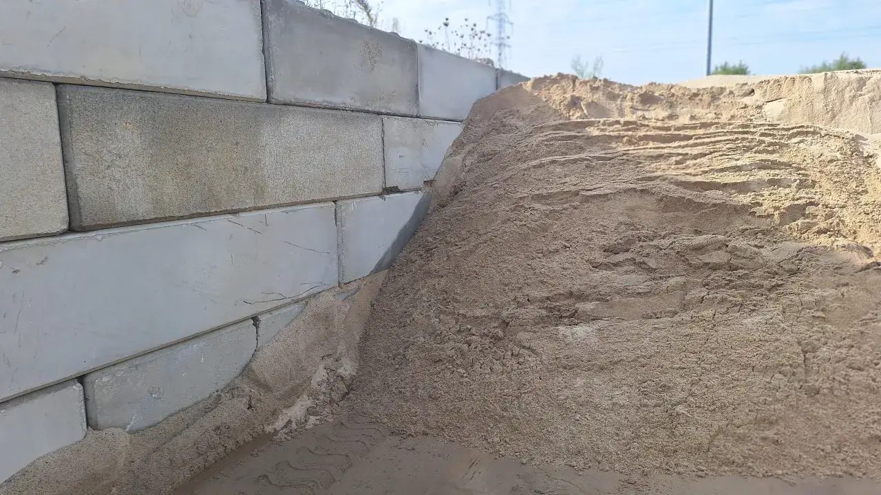 Stos piasku do betonu przylega do betonowych bloków.