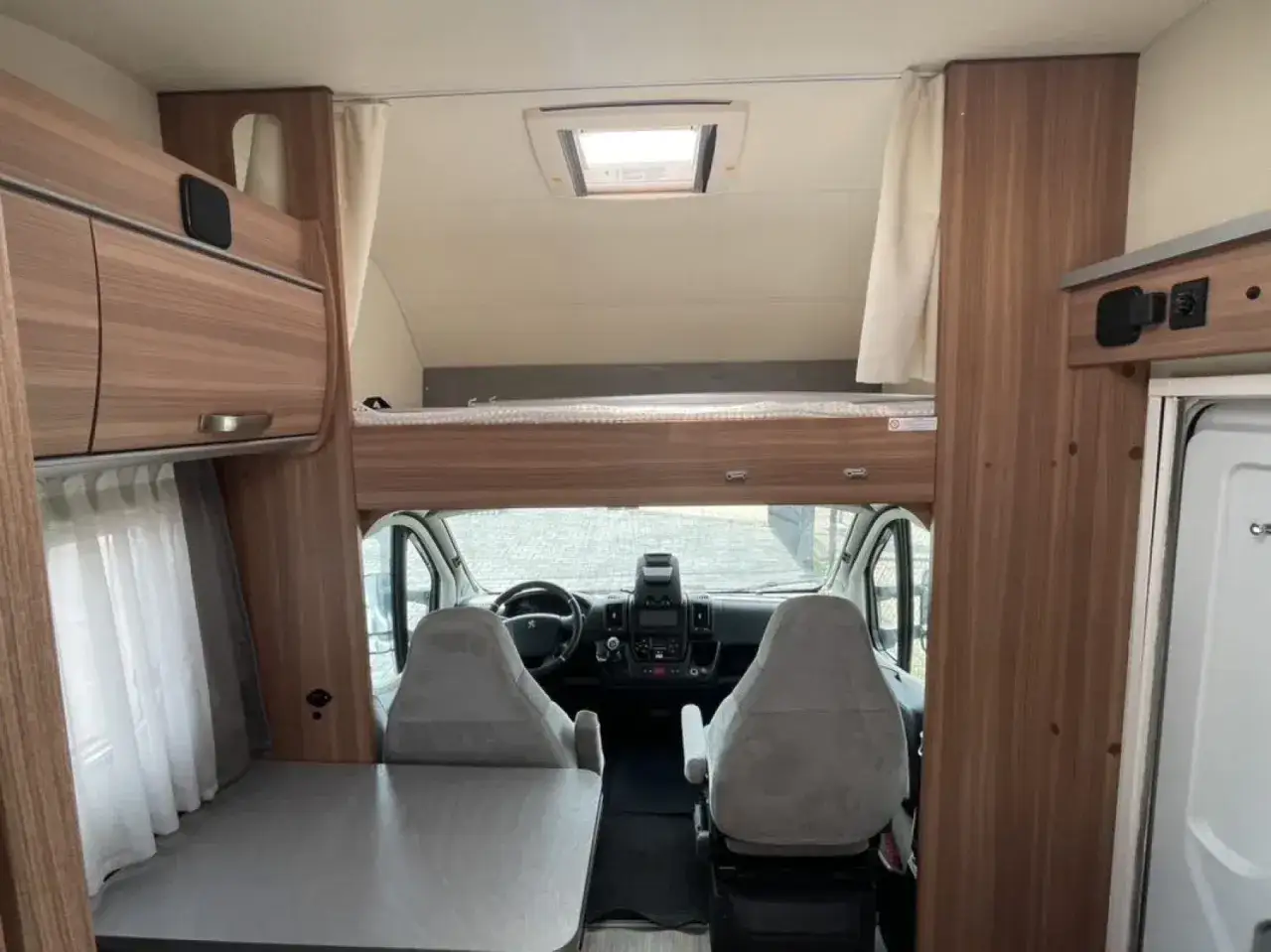 Wnętrze kampera alkowa z łóżkiem nad kabiną, dwoma fotelami i stołem.