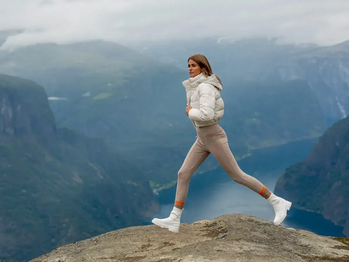 Krótka kurtka puchowa i dopasowane spodnie tworzą stylowy zestaw na tle norweskich fiordów.