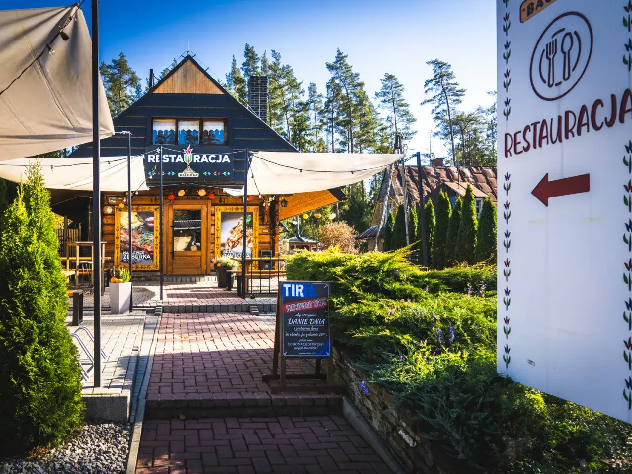 Drewniana restauracja Bac&oacute;wka Chyżne zaprasza na pyszne dania. Znak z czerwoną strzałką wskazuje drogę.