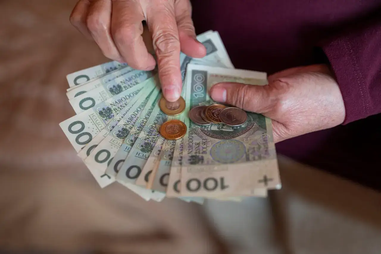 Dłonie liczą banknoty 100 zł i monety. Czy emeryta obowiązuje okres wypowiedzenia przy zmianie świadczenia?