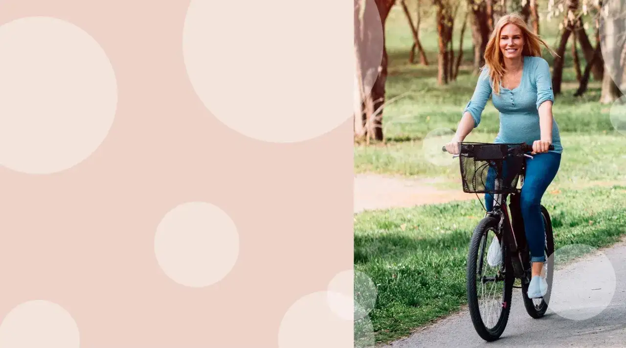 Uśmiechnięta kobieta w ciąży na rowerze w parku.