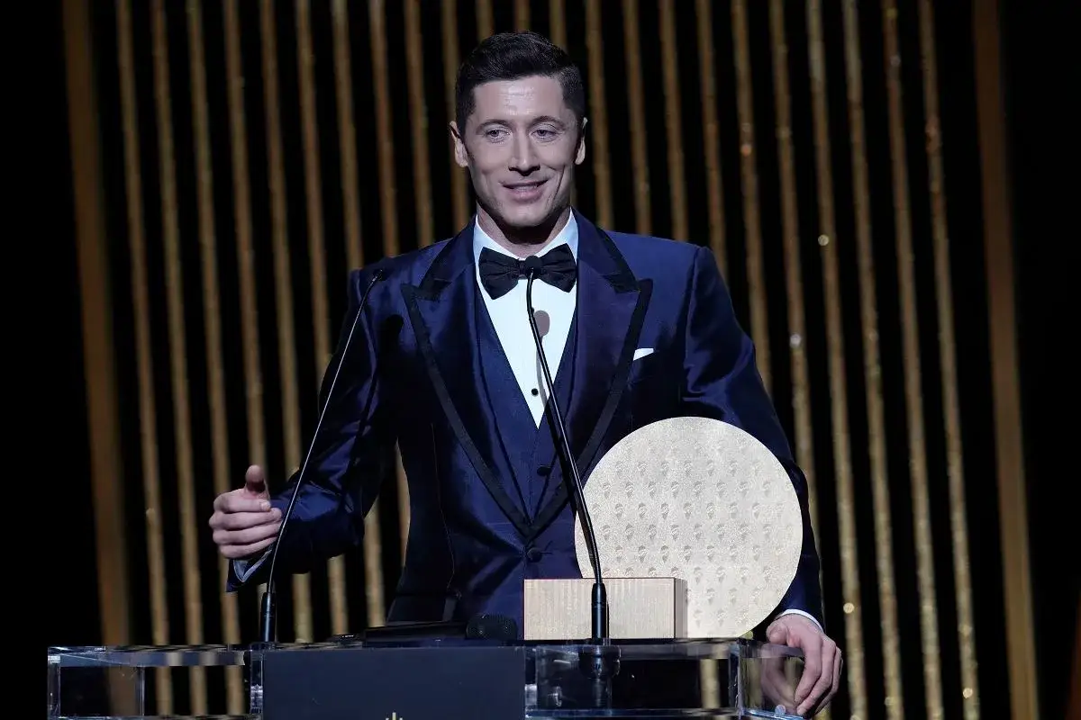 Robert Lewandowski w eleganckim garniturze odbiera nagrodę, gdy jest losowanie złotej piłki.