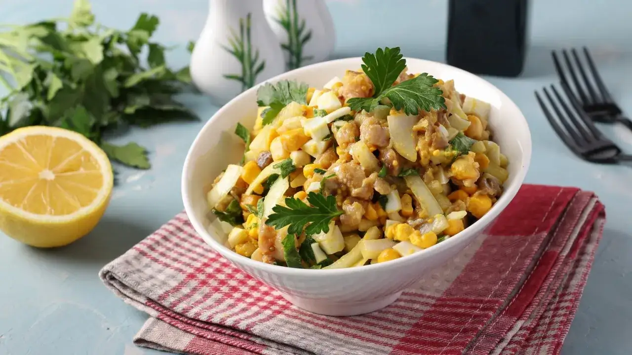 Pyszna sałatka z makreli z jajkiem, kukurydzą i natką pietruszki, podana w białej misce na czerwono-białej serwetce.