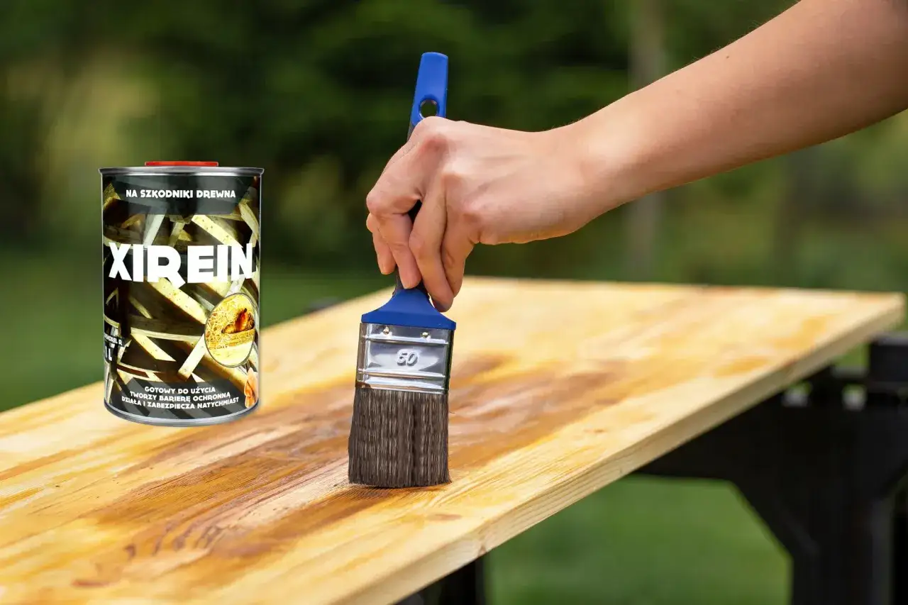 Ręka z pędzlem nakłada impregnat do drewna natryskowy Xirein na drewnianą deskę, chroniąc ją przed szkodnikami.