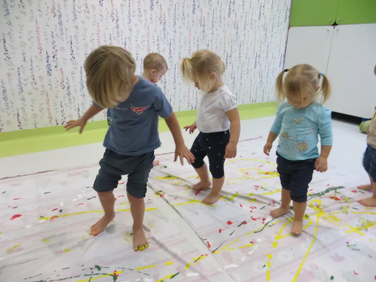 Dzieci malują stopami na wielkim arkuszu papieru. Tak wygląda żłobek pełen kreatywności i zabawy.