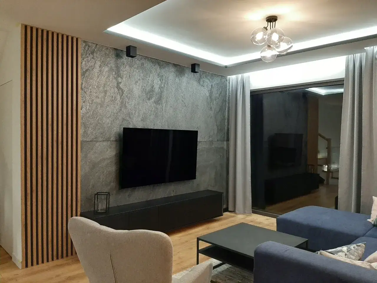 Nowoczesny salon z telewizorem na tle kamiennych płyt ściennych ozdobnych i drewnianych lameli.