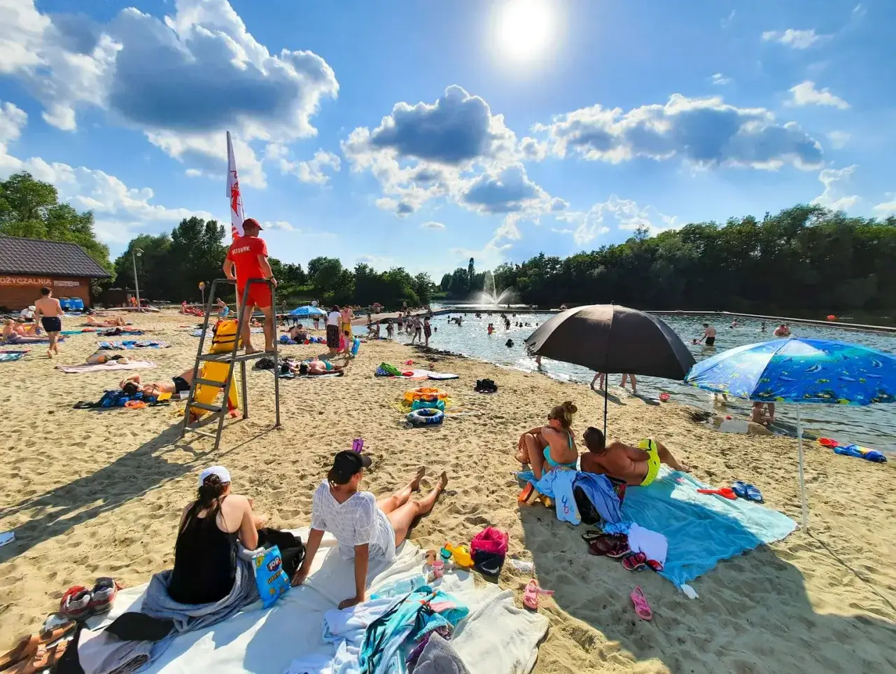 Słoneczny dzień na żwirowni międzyrzec podlaski. Kąpielisko tętni życiem, ratownik czuwa, a plażowicze odpoczywają na piasku.