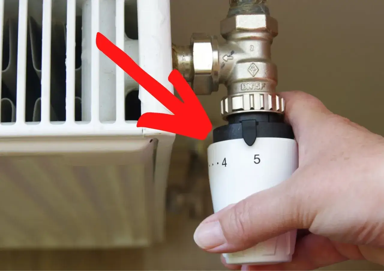 Dłoń reguluje termostat grzejnika, pokazując, jak działa termostat na grzejniku, ustawiając temperaturę.