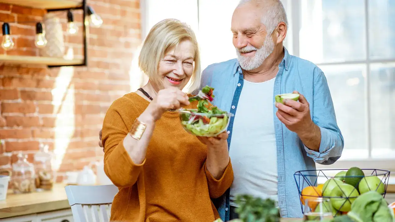 Uśmiechnięci seniorzy przygotowują sałatkę. Zdrowa dieta to klucz, jak wzmocnić starszą osobę.