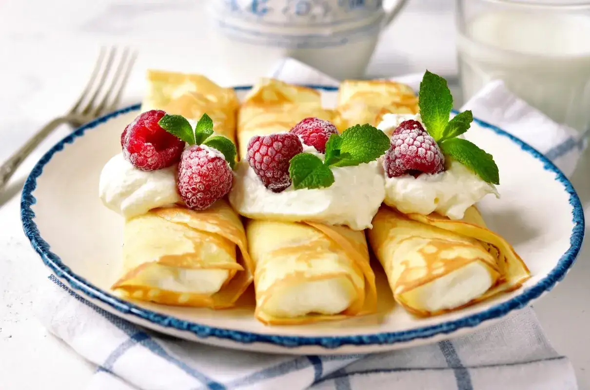 Rolowane naleśniki z serkiem mascarpone, ozdobione malinami i miętą, wyglądają apetycznie.