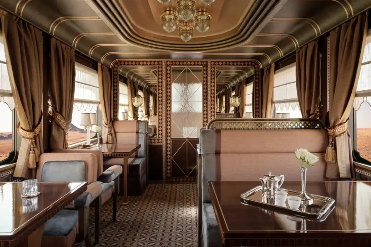 Luksusowe wnętrze wagonu Orient Express. Eleganckie siedzenia, stoliki i lustra tworzą atmosferę podróży przez pustynne krajobrazy.
