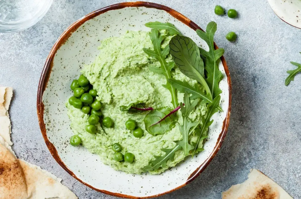 Kremowy zielony groszek dla niemowlaka, udekorowany świeżymi listkami rukoli i buraka. Idealny pierwszy posiłek.