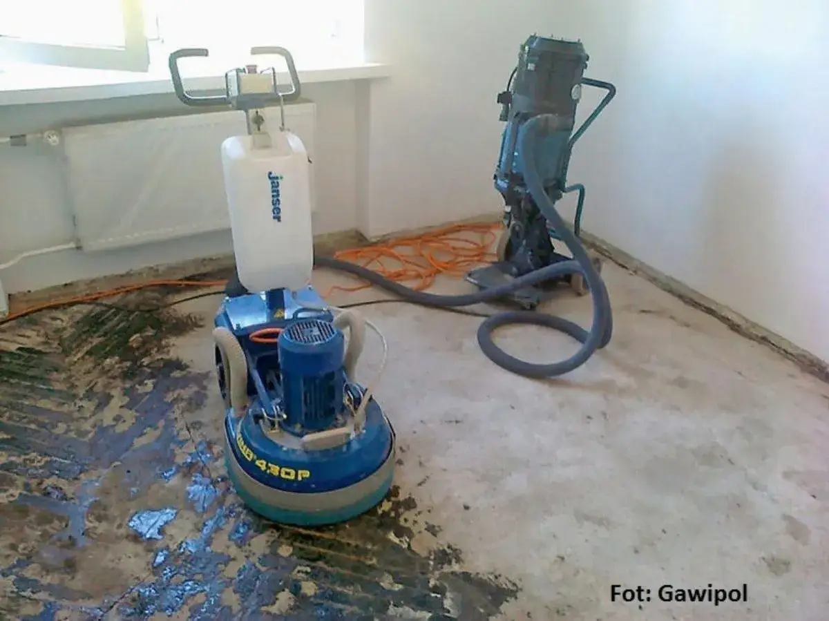 Maszyny do szlifowania posadzki, przygotowujące ją pod parkiet. Jedna z nich to szlifierka Jansen, druga to odkurzacz przemysłowy.
