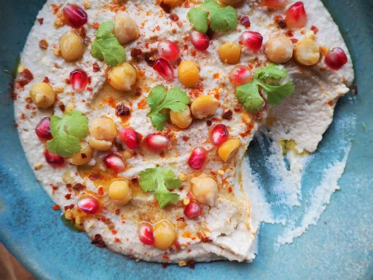 Pyszny hummus z ciecierzycy, udekorowany pestkami granatu, kolendrą i papryką. Idealny na przekąskę.