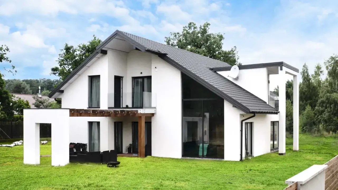 Nowoczesny dom z perlitu, z dużymi przeszkleniami i drewnianą pergolą, otoczony zielonym ogrodem.