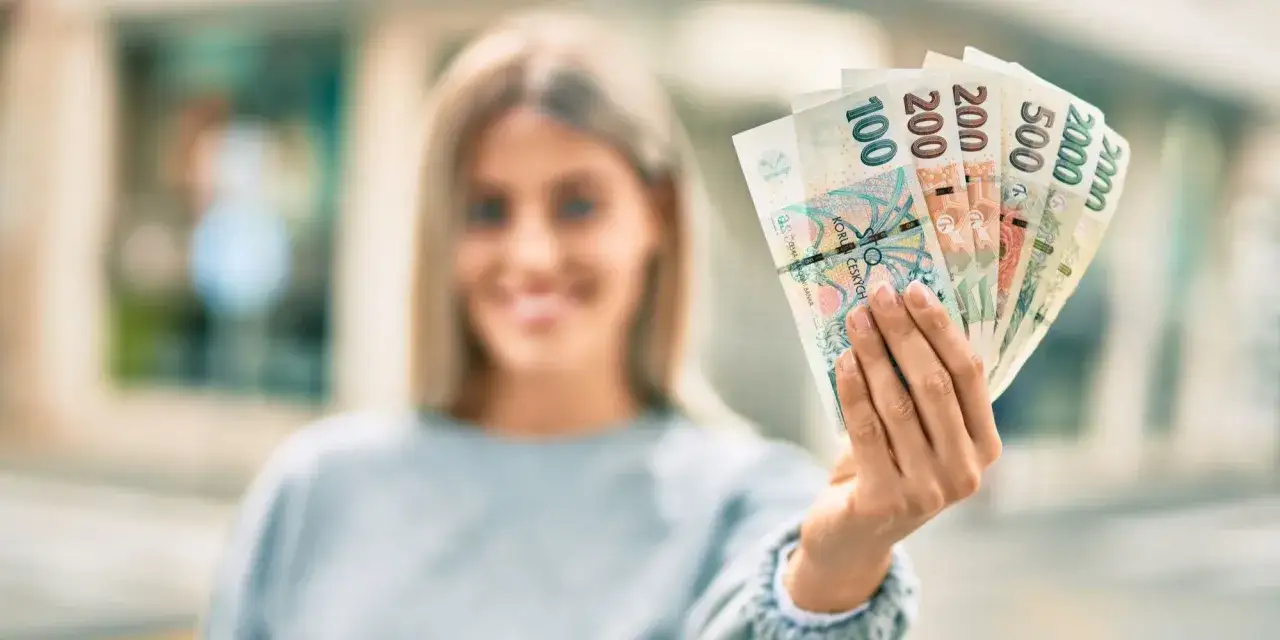 Kobieta trzyma banknoty: 100, 200, 500, 2000 korun českých. To właśnie jaka waluta jest w Czechach.