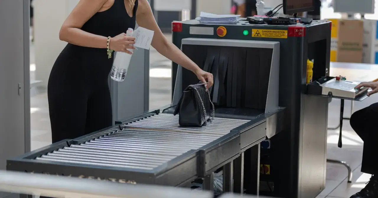 Kobieta kładzie torebkę na taśmociągu przy bramkach bezpieczeństwa, co jest ważnym krokiem, gdy zastanawiasz się, jak przewozić leki w samolocie.