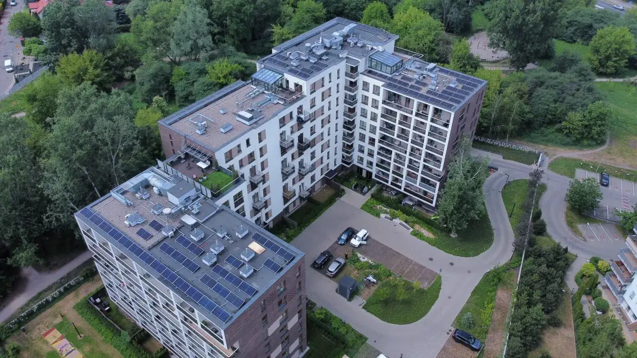 Nowoczesne bloki mieszkalne z panelami fotowoltaika na dachach, otoczone zielenią.