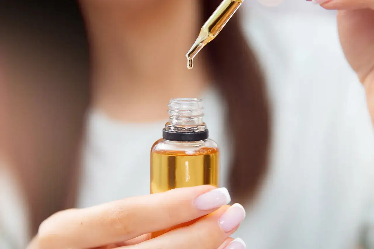Kropla olejku rycynowego spada z pipety do buteleczki. Poznaj, jak stosować olejek rycynowy na włosy dla ich wzmocnienia.