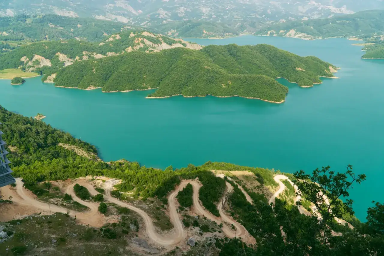 Malowniczy widok na turkusowe wody jeziora Bovilla otoczonego zielonymi wzgórzami. Kręta droga wije się po zboczu.