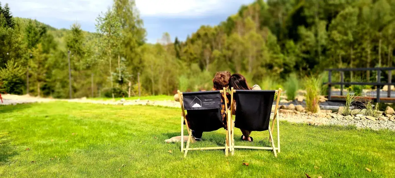 Para odpoczywa na leżakach przed Buk&oacute;wką, luksusową bac&oacute;wką, otoczoną zielenią i g&oacute;rami.
