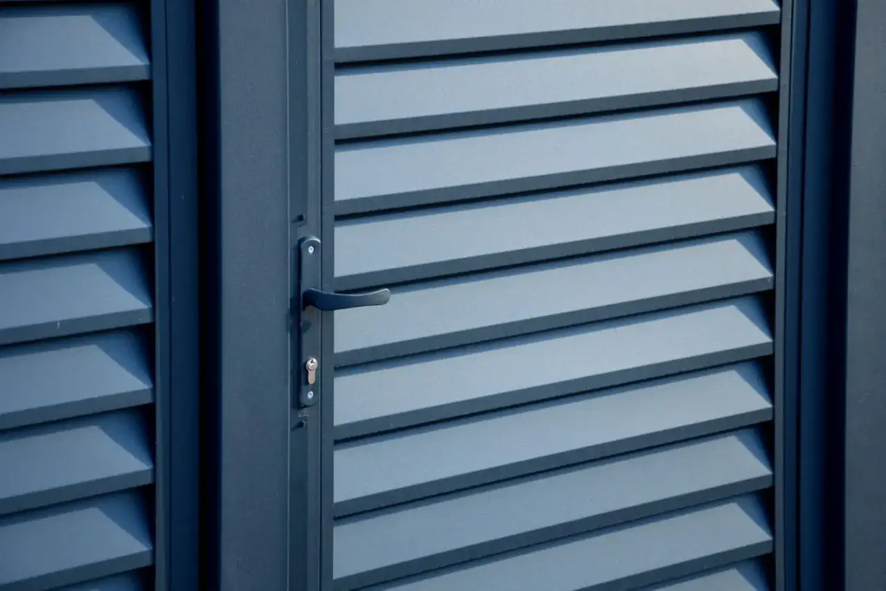 Szara, metalowa futryna z poziomymi żaluzjami i czarną klamką. Dowiedz się, jak odnowić stare futryny metalowe.