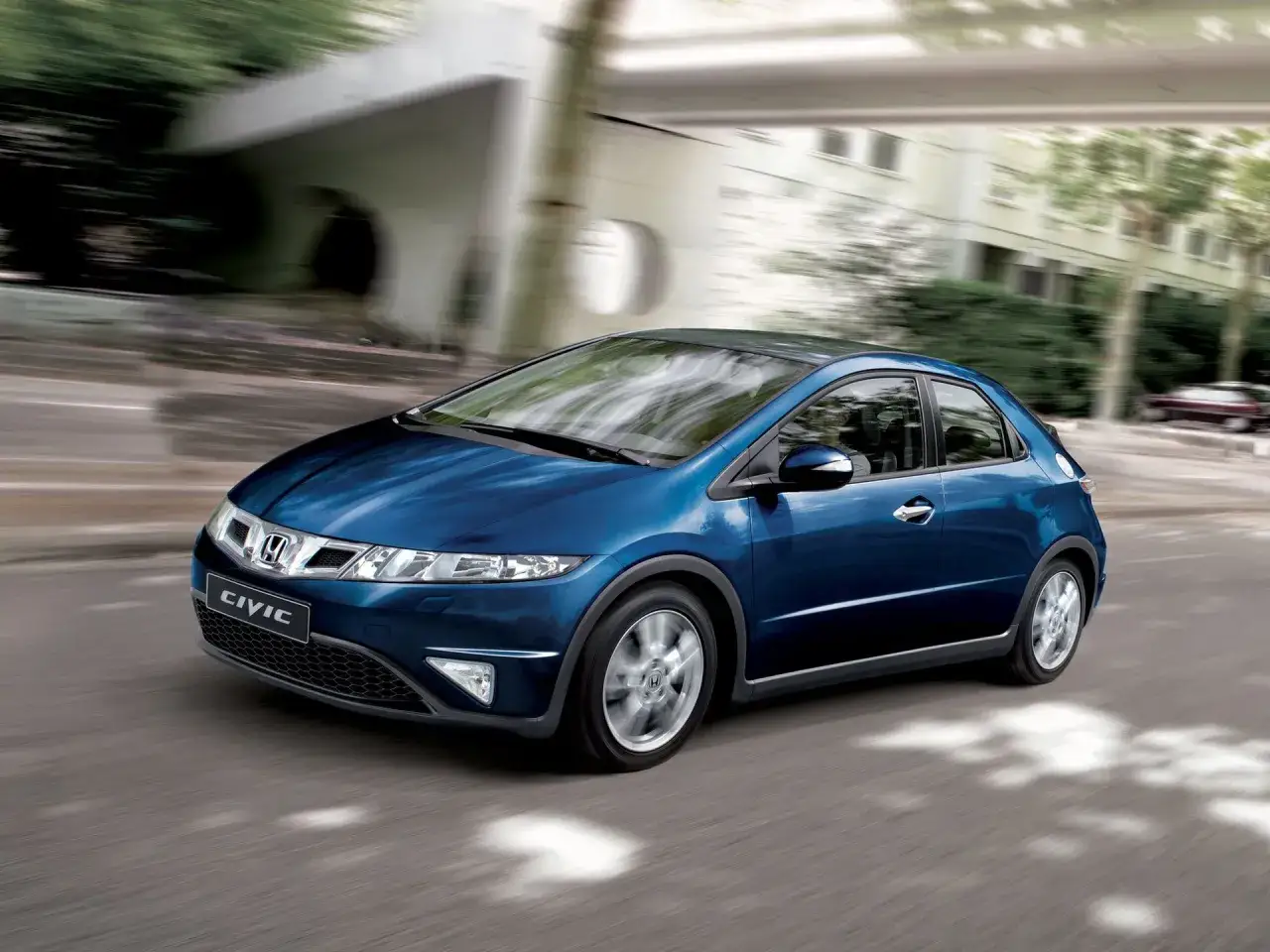 Niebieski Honda Civic, jak UFO, sunie po miejskiej drodze.