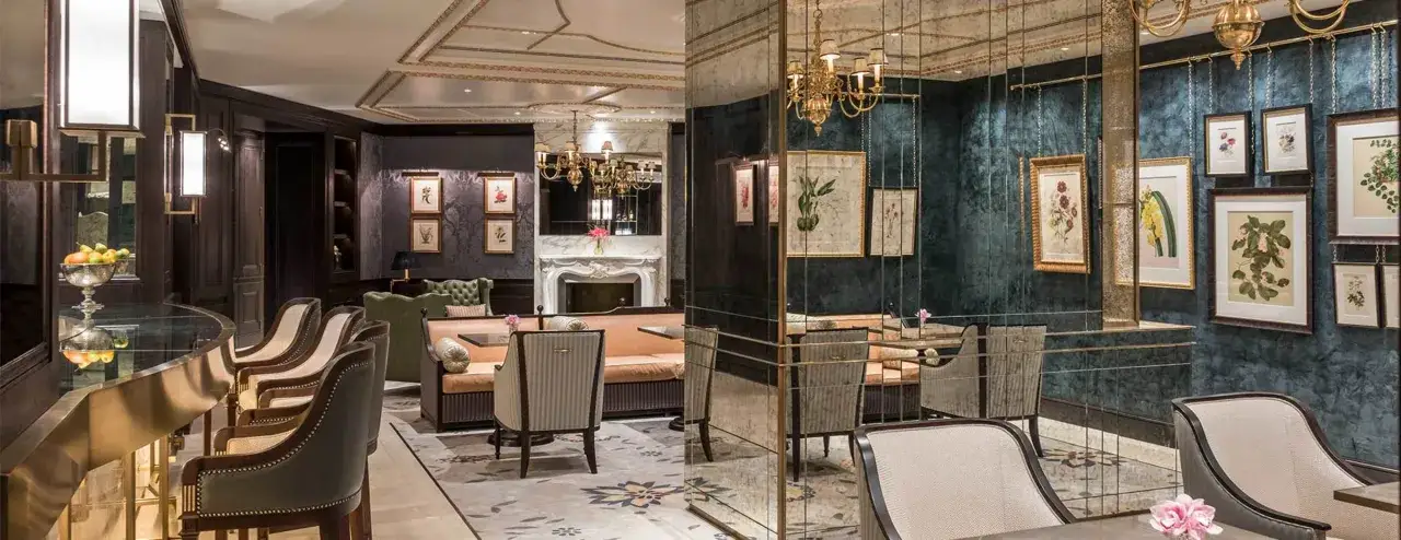 Eleganckie wnętrze luksusowego hotelu z wygodnymi fotelami przy barze, przytulną strefą wypoczynkową z kanapami i kominkiem, ozdobione botanicznymi obrazami.